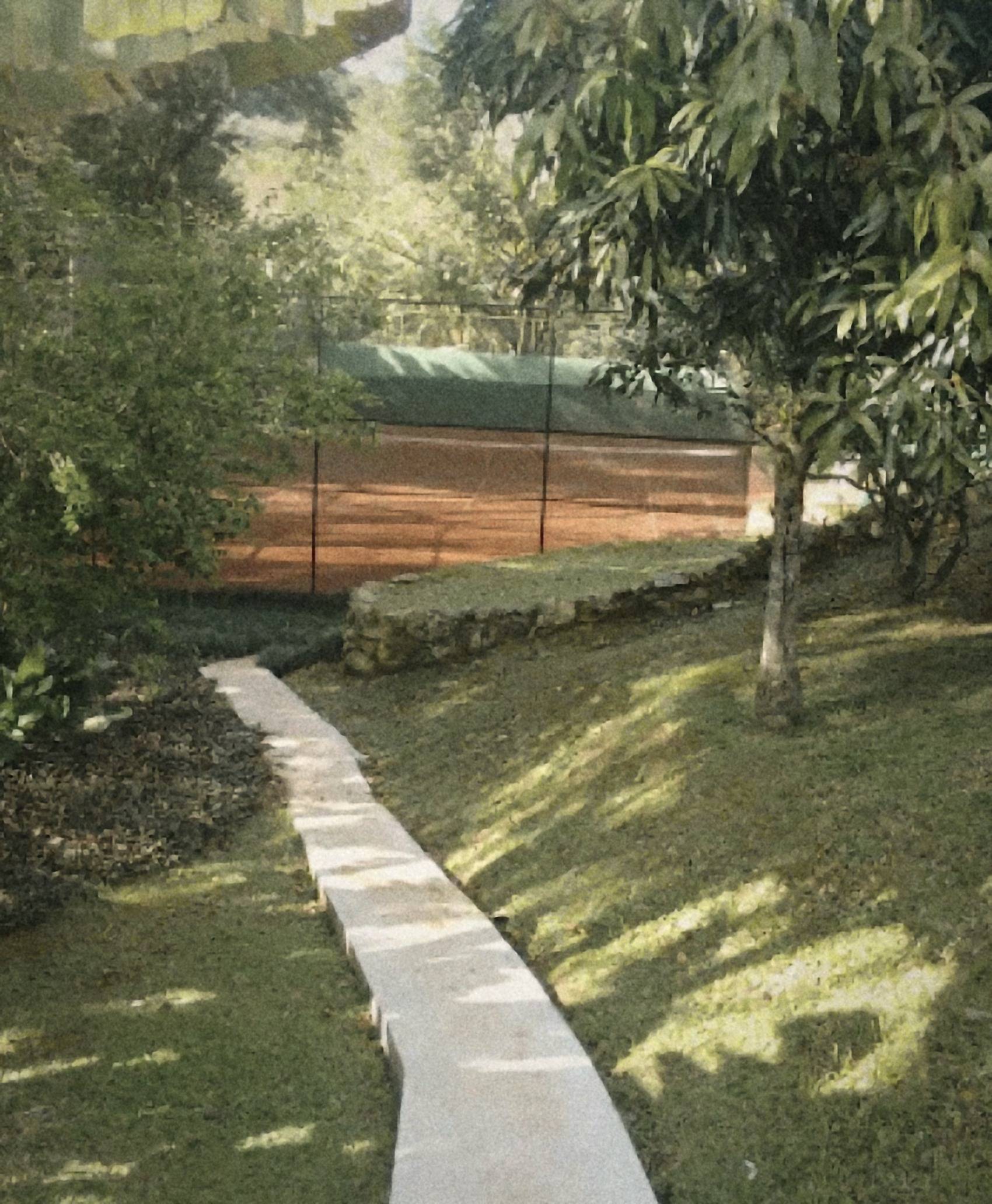 Caminho de pedra descendo pelo gramado sombreado até a quadra de saibro, com a mata ao fundo.